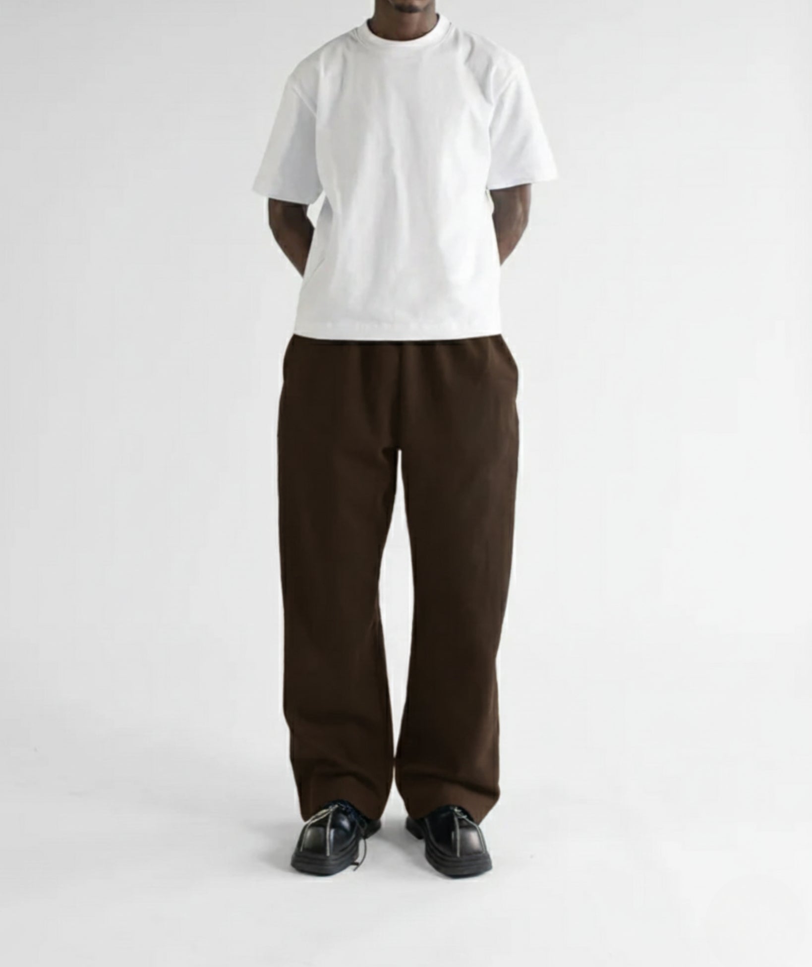 Model standing with hands in pockets, wearing dark brown straight-leg sweatpants to show the relaxed fit and drape.